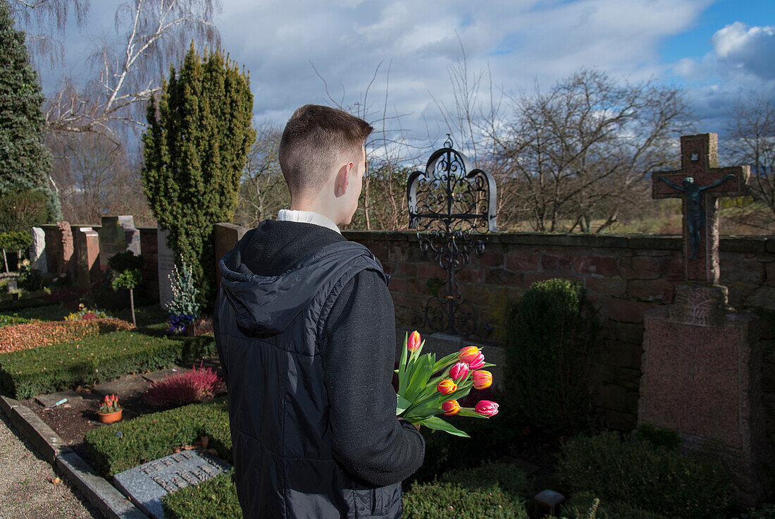 Teenager with Tulips Standing in front of Grave Stones in Cemetery