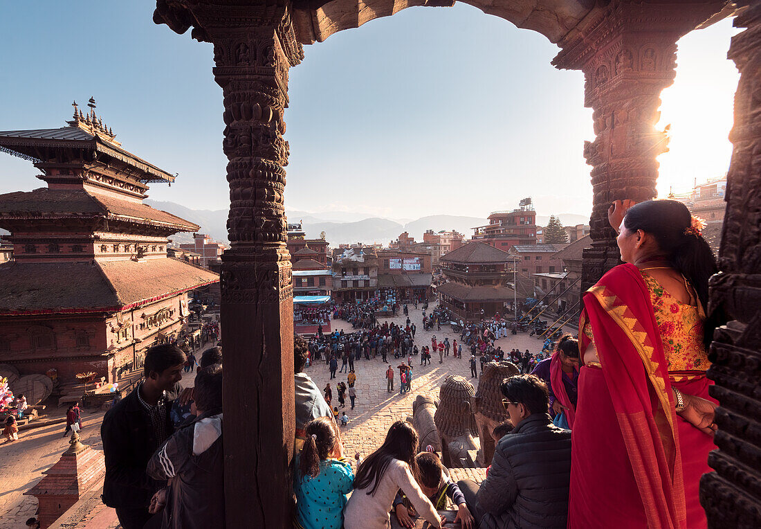 Einheimische in farbenfroher Kleidung genießen einen sonnigen Festtag rund um die Tempel und Architektur von Bhaktapur, Nepal, Asien