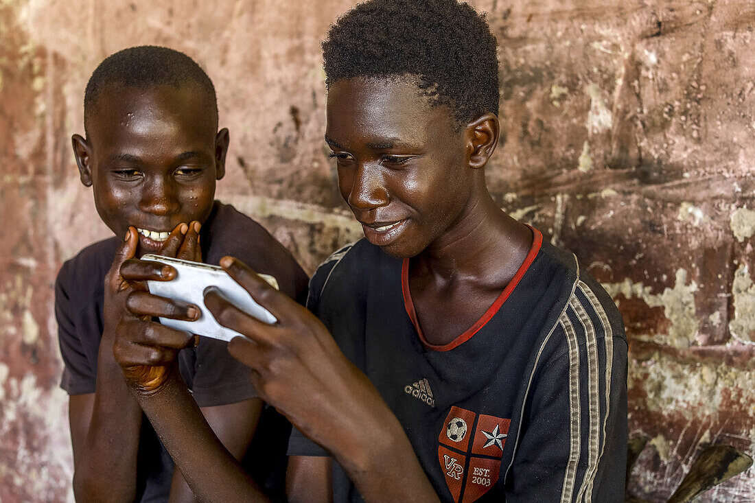 Lehrlinge benutzen ein Mobiltelefon in einer Werkstatt in Fatick, Senegal, Westafrika, Afrika