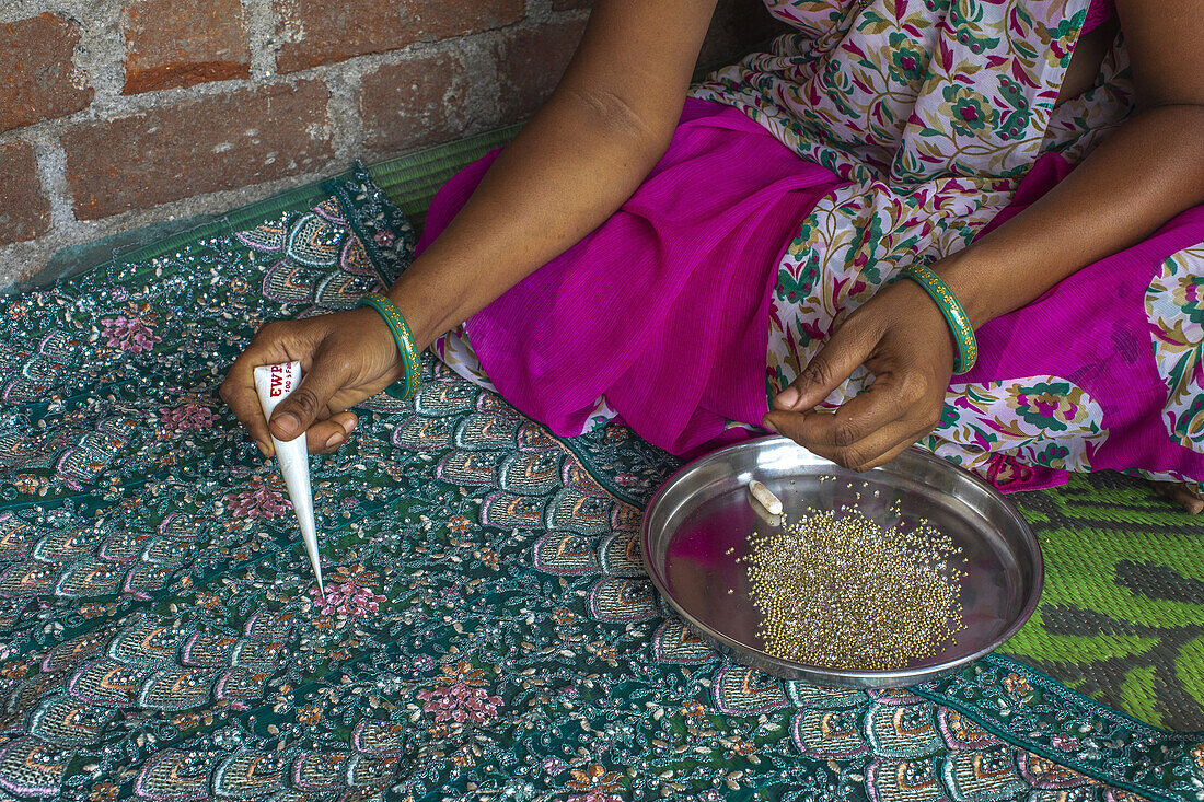 Adivasi-Frau klebt Perlen auf einen Sari in einem Dorf im Narmada-Distrikt, Gujarat, Indien, Asien