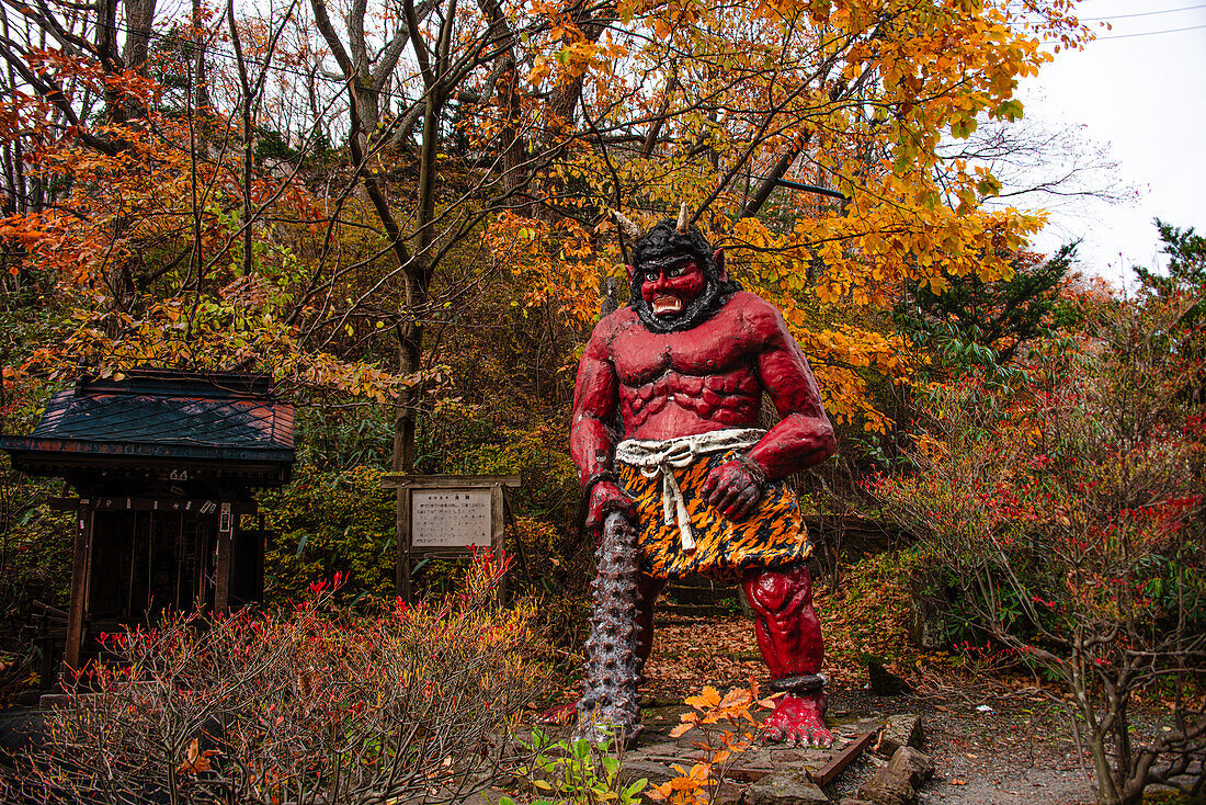 Stehende rote Dämonenstatue mit einer großen Keule im Herbstwald, Noboribetsu, Hokkaido, Japan, Asien