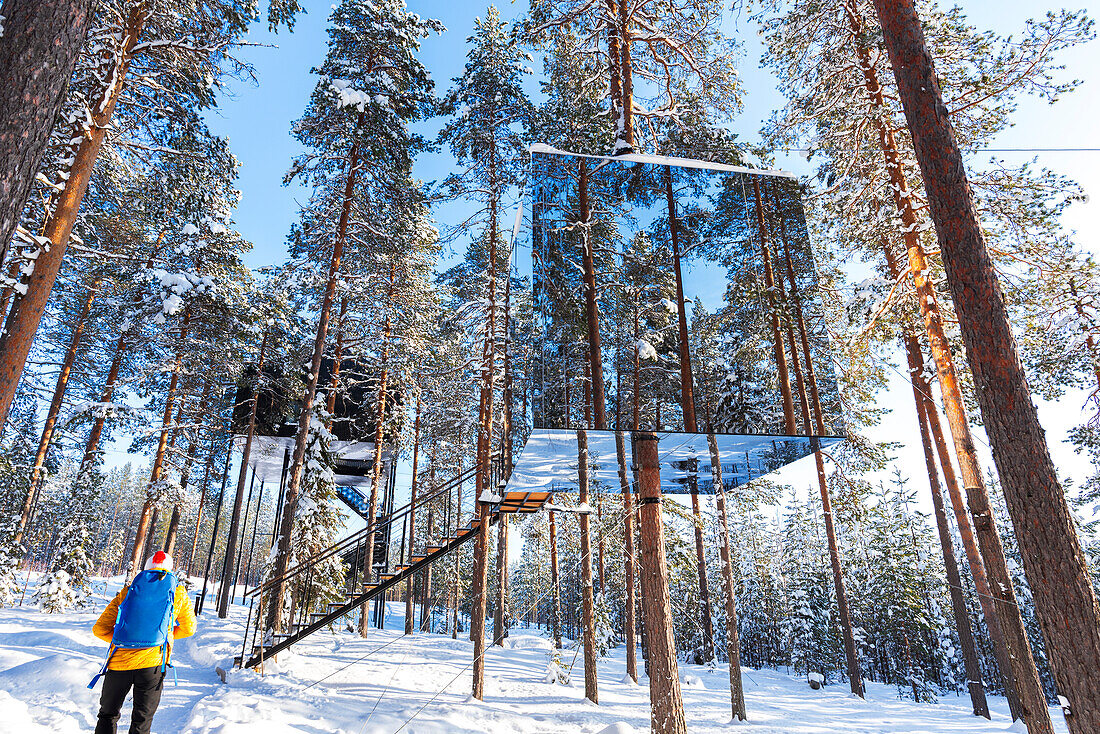 View of a tourist admiring the cube shaped room with mirror wall inside a boreal forest covered with ice and snow,Tree hotel,Harads,Lapland,Sweden,Scandinavia,Europe