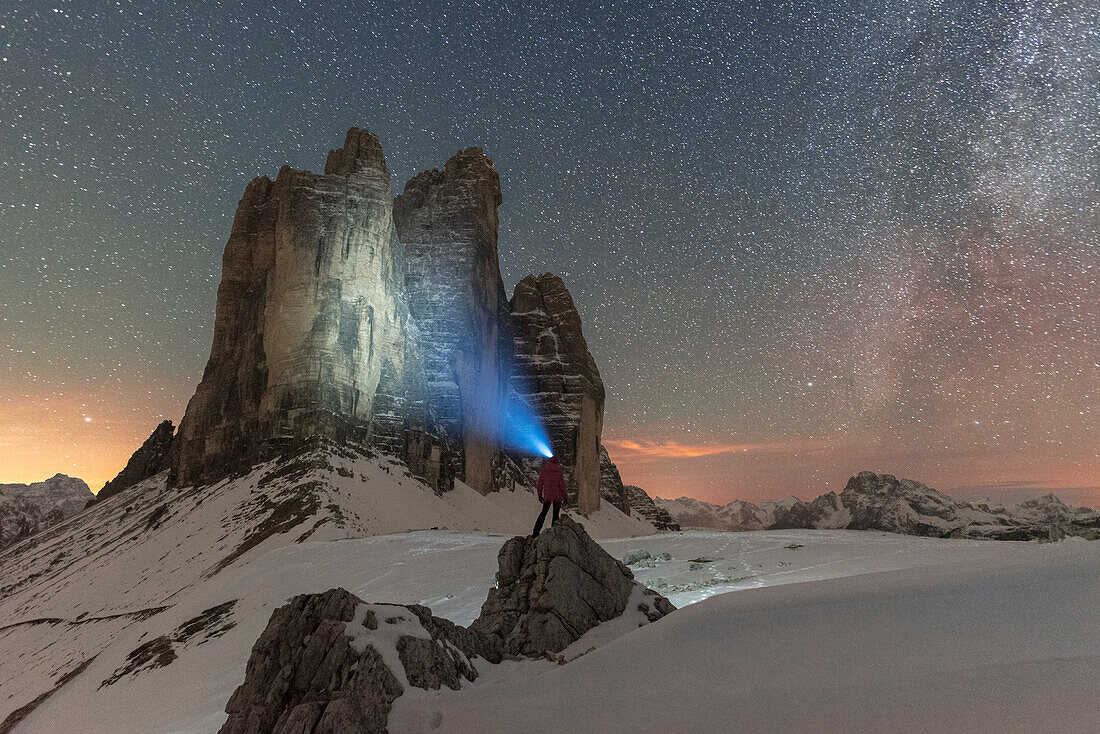 Wanderer mit Stirnlampe betrachtet die Drei Zinnen in einer sternenklaren Nacht mit der Milchstraße, Winterblick, Drei Zinnen, Sexten, Dolomiten, Südtirol, Italien, Europa