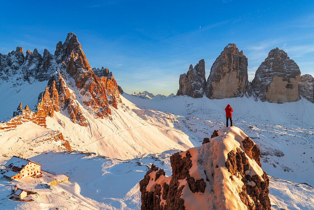 Rückansicht eines Wanderers, der die Drei Zinnen vom Gipfel eines riesigen Felsens aus bewundert, Winteransicht, Sexten, Dolomiten, Südtirol, Italien, Europa