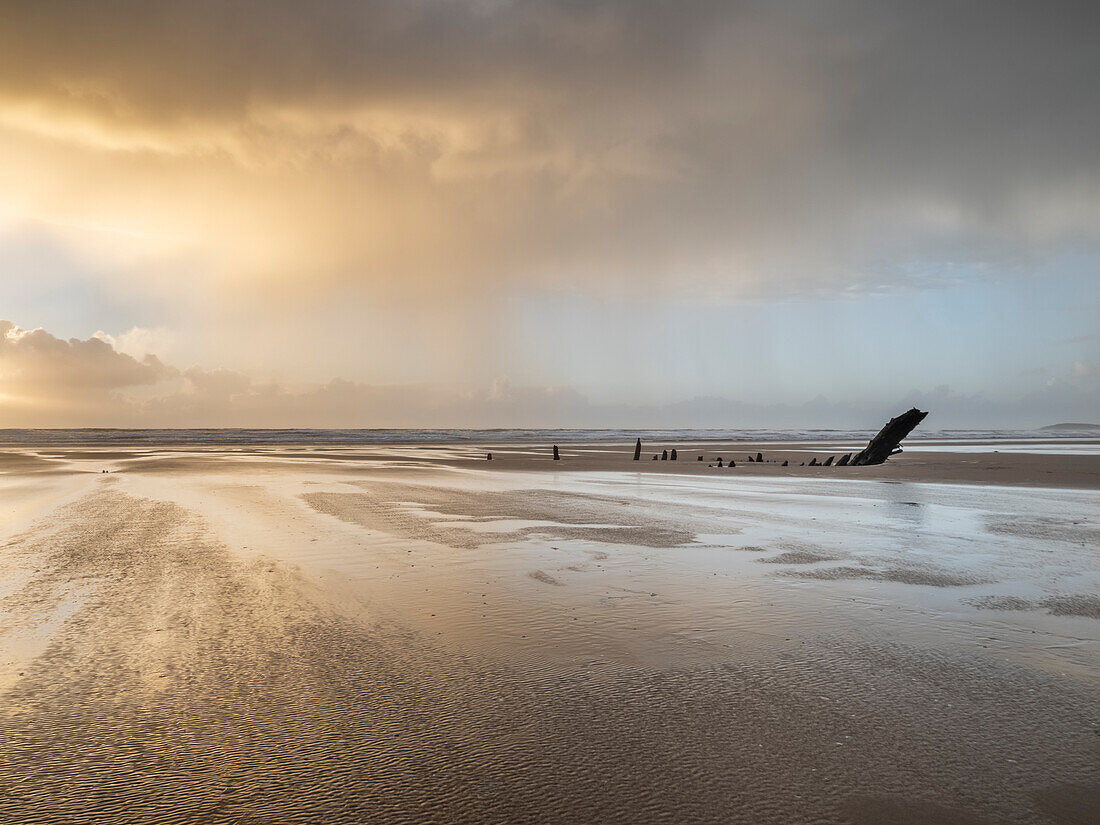 Rain sweeping across Rhossili at sunset showing the shipwreck of the Helvetia,Rhossili,Gower,South Wales,United Kingdom,Europe