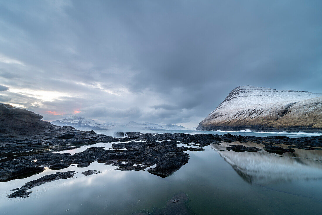 Schneebedeckte Berge und Felsbecken bei Ebbe, Dorf Gjogv, Eysturoy Island, Färöer Inseln, Dänemark, Europa