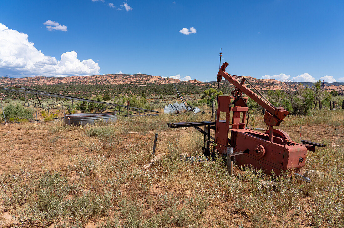 Eine alte mechanische Pumpe an einem Wasserbrunnen auf einer ehemaligen Rinderfarm im Südosten von Utah. Dahinter befindet sich eine zusammengebrochene Windpumpe oder Windmühle.