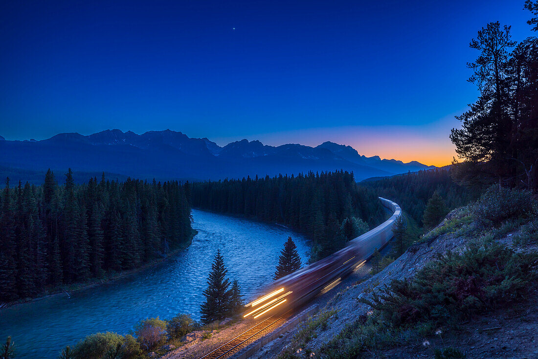Ein CPR-Güterzug auf dem Weg nach Osten durch die kanadischen Rocky Mountains, in der Abenddämmerung mit der hellen Venus am westlichen Himmel über den Gipfeln der kontinentalen Wasserscheide.