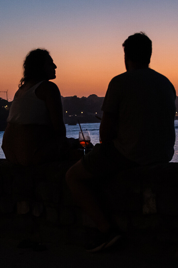 Ein Paar genießt einen Drink bei Sonnenuntergang auf der Promenade Jacques Thibaud vor dem Strand Grande Plage von Saint Jean de Luz, einem Fischerdorf an der Mündung des Flusses Nivelle im südwestfranzösischen Baskenland