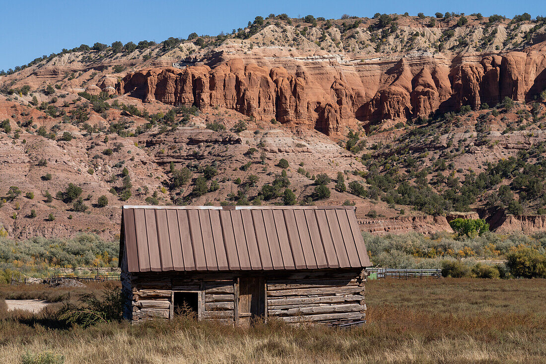 Eine alte Blockhütte auf einer Ranch in der Nähe von Cannonville im Südwesten Utahs mit erodierten Sandsteinklippen im Hintergrund.