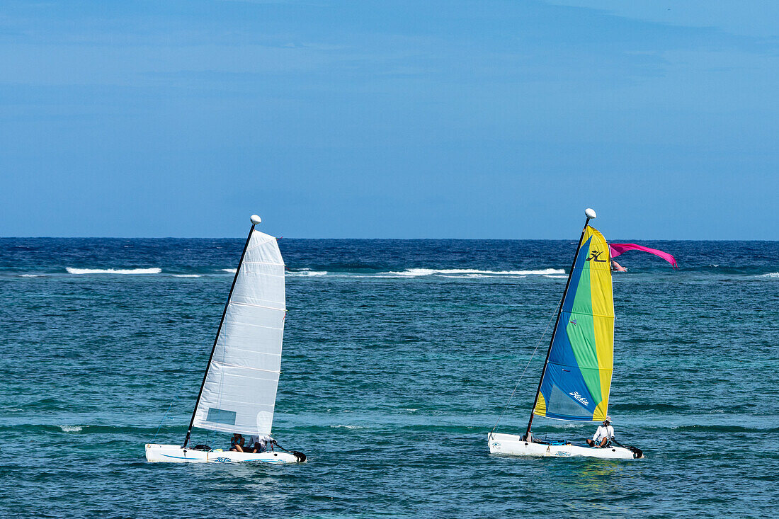 Hobie Cat catamaran sailboats sailing in the Caribbean Sea at San Pedro on Ambergris Caye in Belize. The wave break at the Belize Barrier Reef is visible behind.