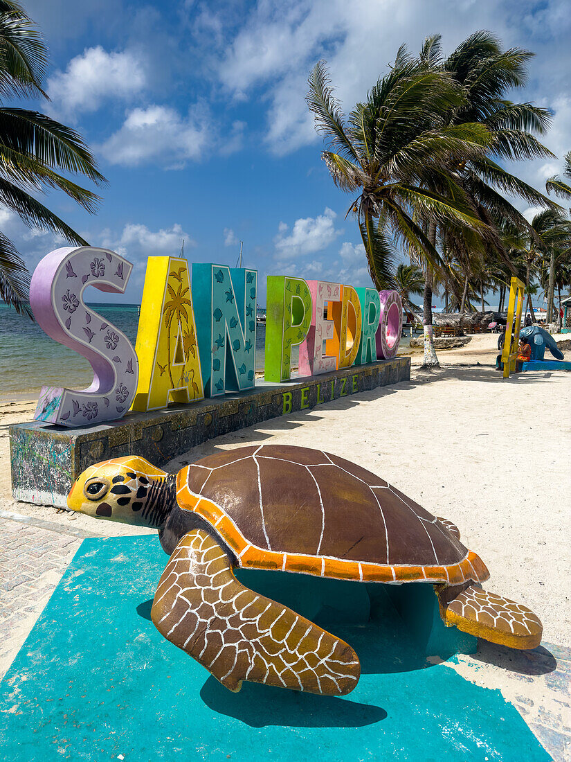 Palmen und eine Meeresschildkrötenstatue vor einem 3-D-Schild am Strand von San Pedro auf Ambergris Caye, Belize.
