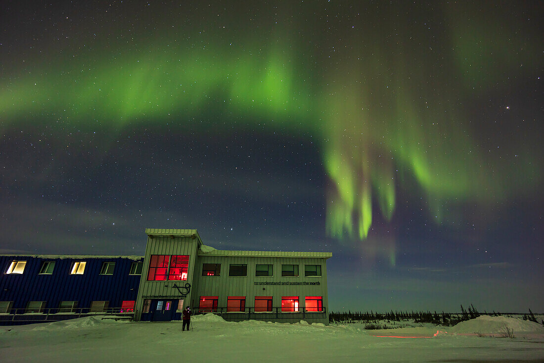 Auroral curtains in the north over the Churchill Northern Studies Centre,with a lone photographer setting up. This was February 25,2023 from the parking lot.