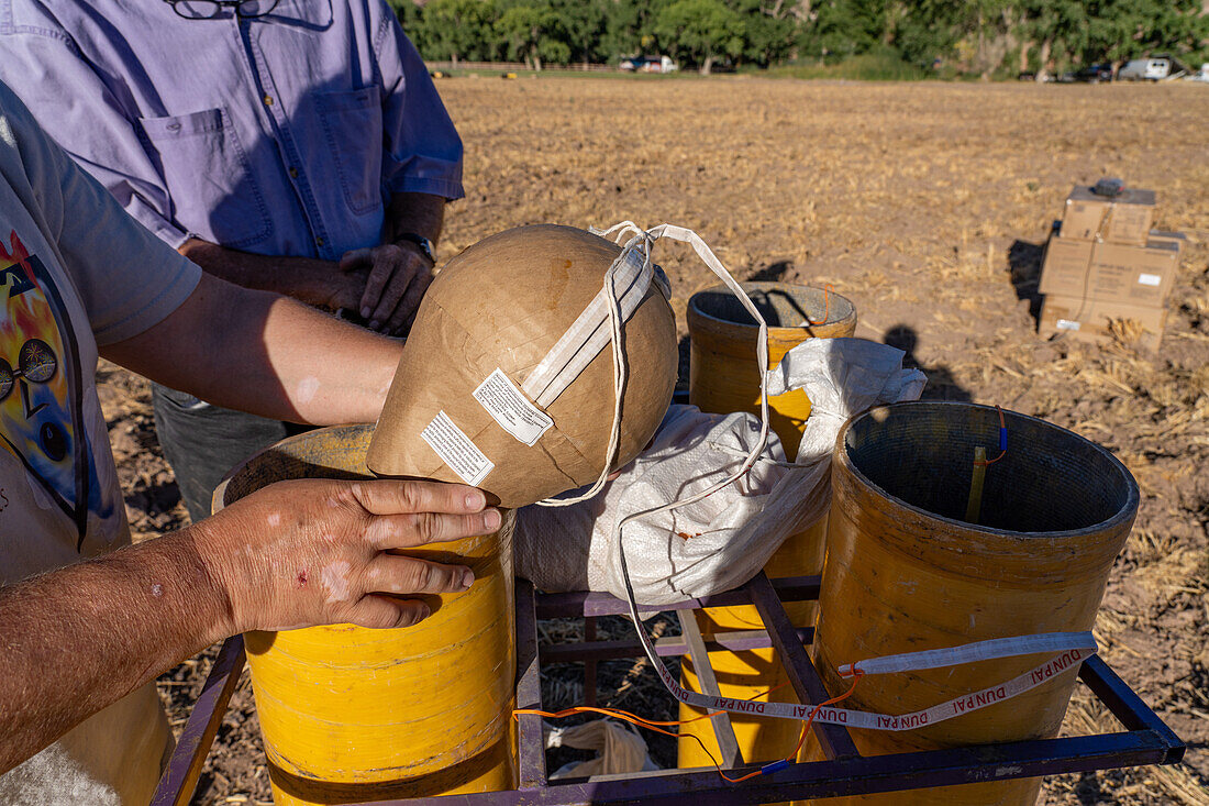 Technicians examine an 8" pyrotechnic shell being prepared for a fireworks show in a field in Utah.