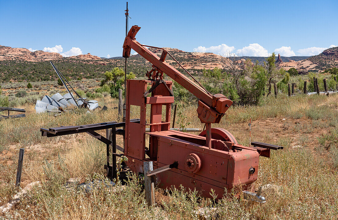 Eine alte mechanische Pumpe an einem Wasserbrunnen auf einer ehemaligen Rinderfarm im Südosten von Utah. Dahinter befindet sich eine zusammengebrochene Windpumpe oder Windmühle.