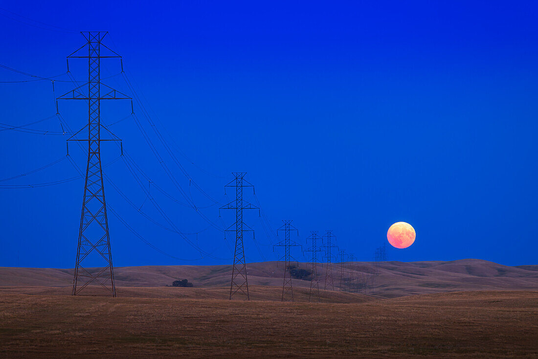 The Full Moon of July 31,2023 rising at the end of a long line of high tension towers across the prairie near Milo,Alberta. Some smoke in the air made the rising Moon even redder than normal,making it look like an eclipsed Moon. This night the alignment of the rising point of the Full Moon coincided with the angle of the powerlines off to the southeast at 135° azimuth.