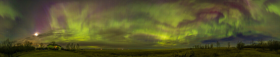 Ein 330°-Panorama der großen April-Aurora-Show am 23. April 2023, aufgenommen von zu Hause in Süd-Alberta. Eine andere Kamera ist in der Szene und macht einen Zeitraffer. Norden ist links von der Mitte; Osten rechts von der Mitte; Süden ist rechts; . Die Mondsichel und die Venus gehen im Westen unter, ganz links in den Wolken.