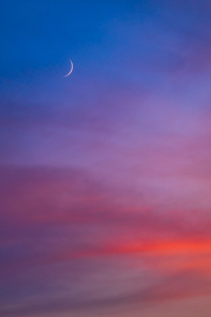 Die zunehmende 3 Tage alte Mondsichel vom 20. Juli 2023 inmitten der Farben eines späten Sonnenuntergangs.