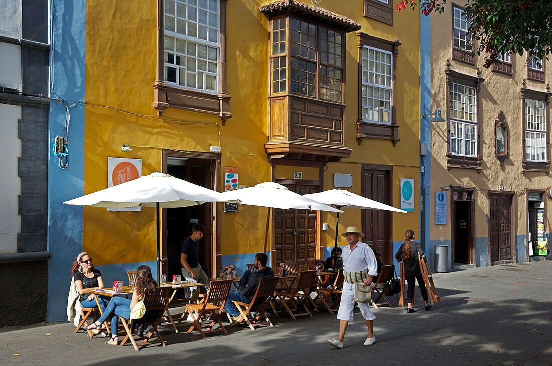 Spain, Canary Islands, Tenerife Island, La Laguna, man in traditional Canarian costume in front of a cafe terrace and a colonial house with yellow facade and wooden balcony