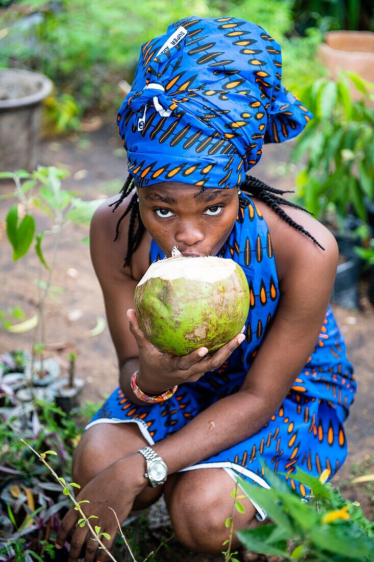 Benin, Cotonou, Frau trinkt eine Kokosnuss