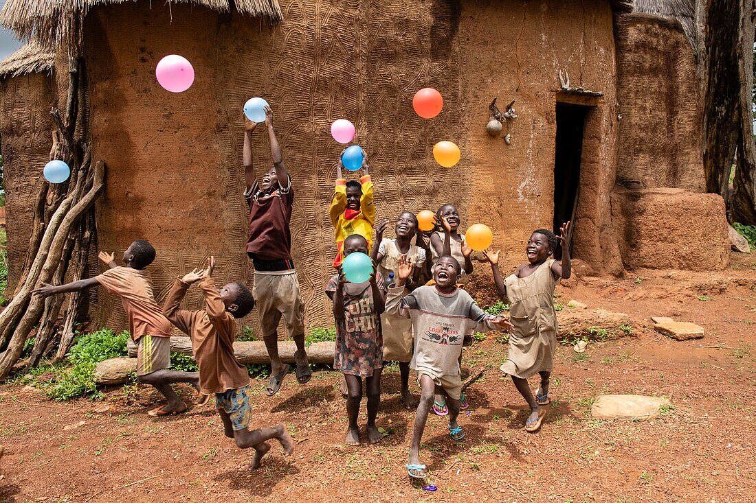 Benin, Nothern distict, Atacora mountains area, Koussoukoingou, children playing with ballons in front of a Tata made with banco (soil mixed with straw), traditional defensive two-storey habitat typical of northern Benin