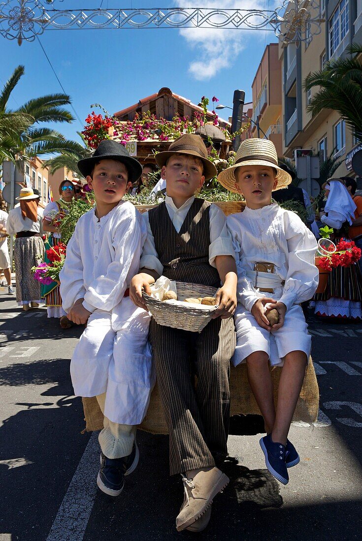 Spanien, Kanarische Inseln, Insel Teneriffa, Kinder in traditioneller kanarischer Tracht sitzen auf einem geschmückten Festwagen während einer romería, einem traditionellen Fest