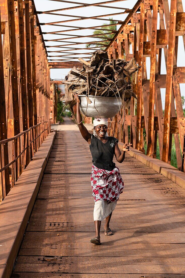 Benin, Grand Popo, woman carrying barks on her head on the old bridge