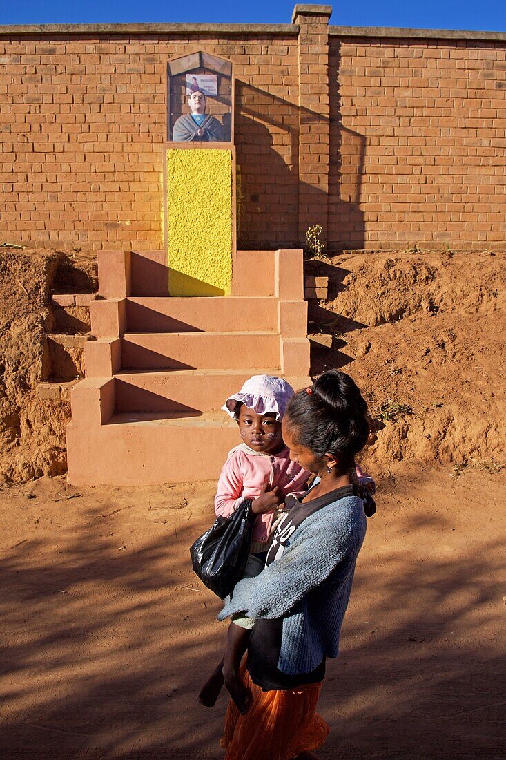 Madagascar, Analamanga, Ambohidrazaka, a woman with her baby in front of a Catholic religious status