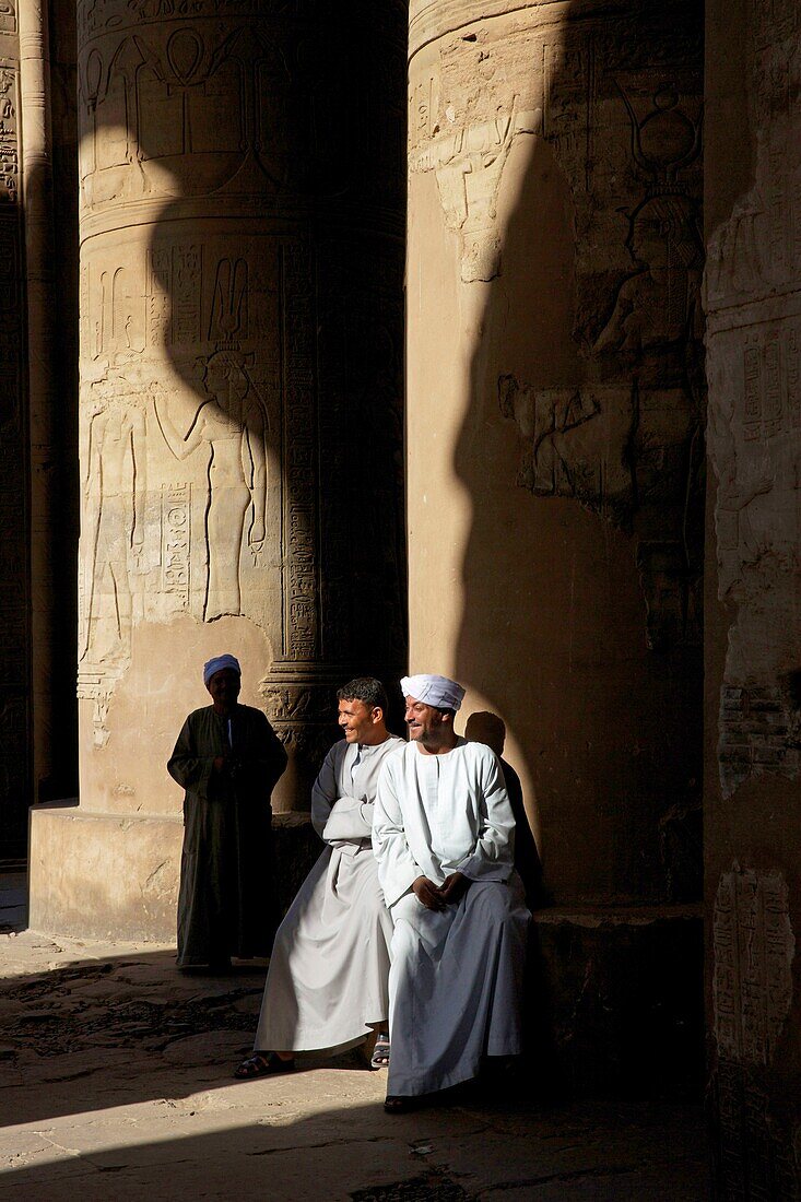 Ägypten,Oberägypten,Niltal,Kom Ombo,Turbanbedeckte Tempelwächter schauen amüsiert auf den Fuß einer Säule des Kom Ombo Tempels zwischen Schatten und Licht