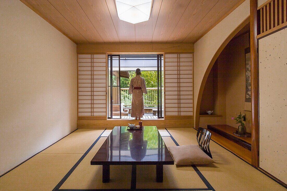 Japan, Kyushu island, Kumamoto region, Kurokawa Onsen, Ryokan Okunoyu, traditional luxury inn located in a spa town, young Asian woman in kimono, standing up, in front of the balcony door of her room