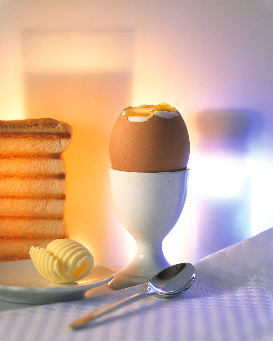 Aufgeschlagenes Frühstücksei, daneben Butterflocke, Toast