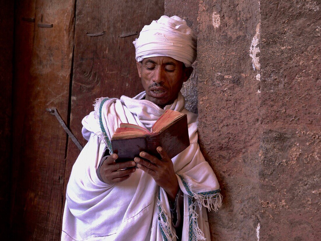 Ethiopia, Amhara region, a man dressed in white reads prayers in front of a Lalibela church