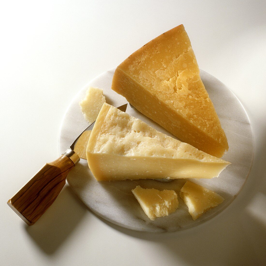 Pieces of parmesan with cheese knife on round marble slab