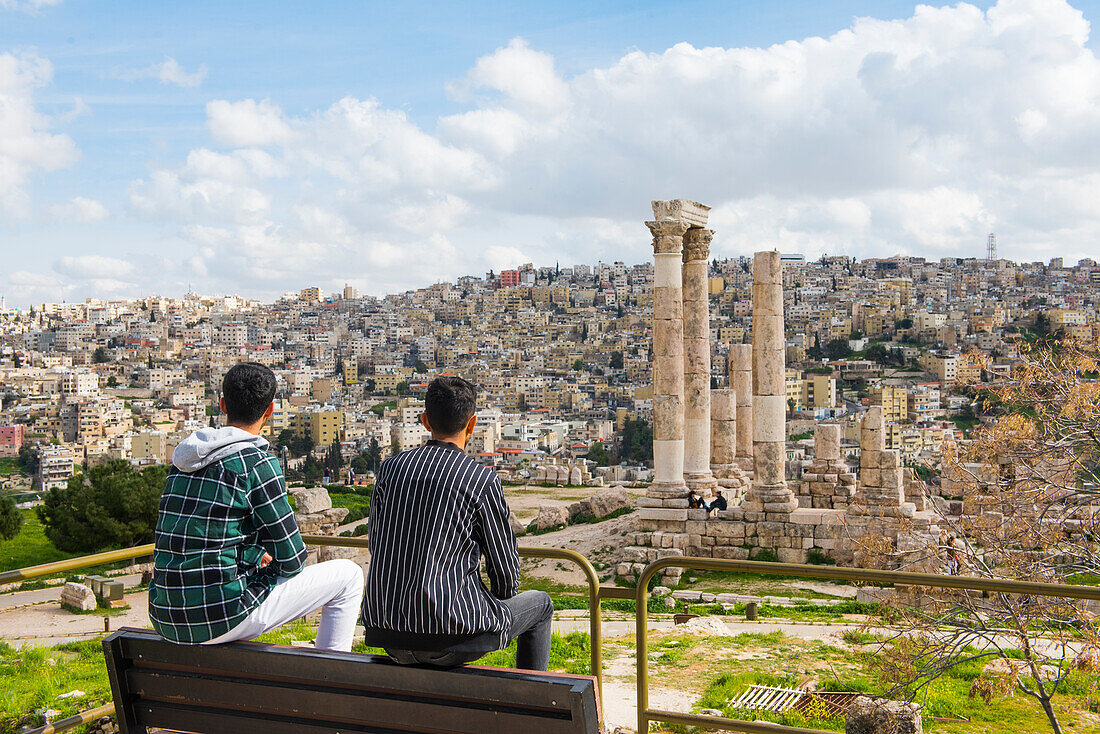 Zwei junge jordanische Männer sitzen auf einer Bank gegenüber dem Herkules-Tempel in der Zitadelle von Amman (Jabal al-Qal'a),einer historischen Stätte auf einem Hügel im Herzen von Amman,Jordanien,Naher Osten