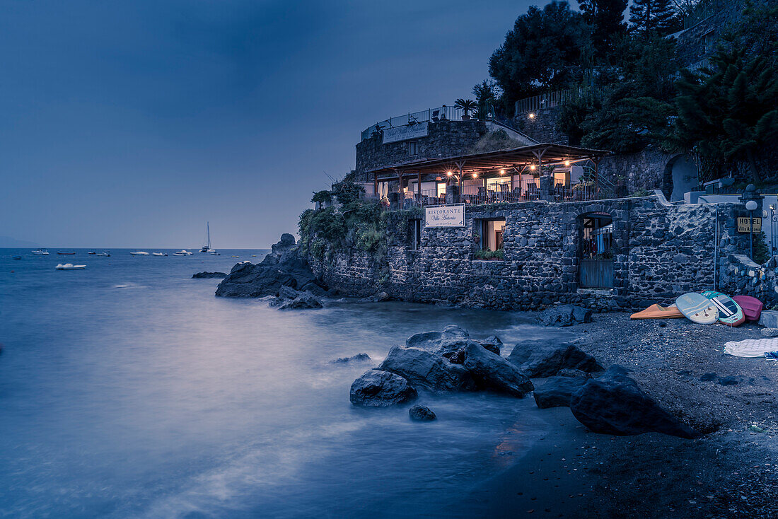 View of coastline restaurant near Aragonese Castle at dusk, Port of Ischia, Island of Ischia, Campania, Italy, Europe