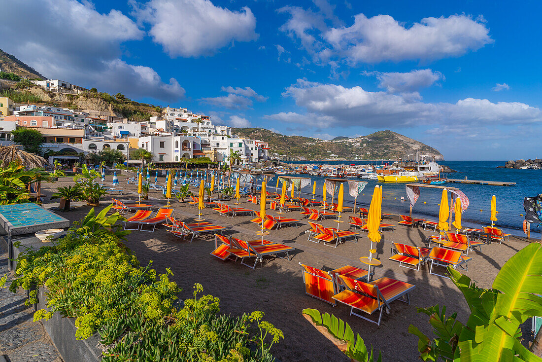 View of brightly coloured loungers on the beach and Sant'Angelo from Porto di Sant'Angelo, Sant'Angelo, Island of Ischia, Campania, Italy, Europe