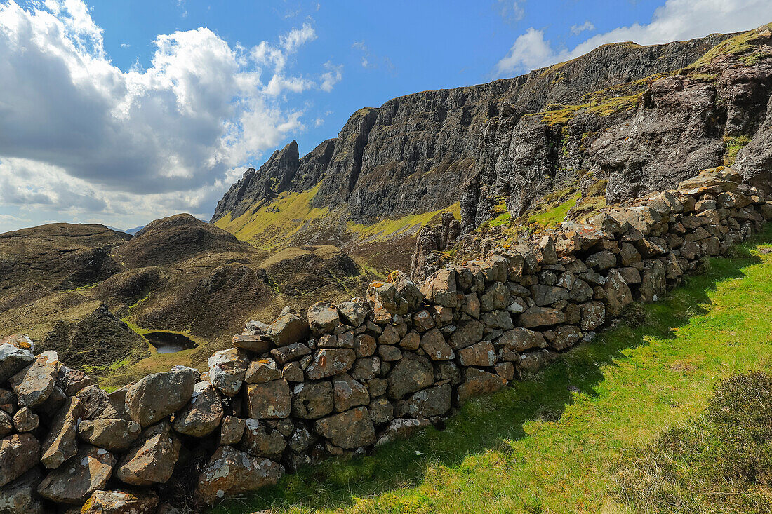 Dry stone wall and towering cliffs of basalt lava over Jurassic sediments at the Quiraing, a famous hike and scenic attraction in the far north east of the island, Quiraing, Staffin, Skye, Inner Hebrides, Scotland, United Kingdom, Europe