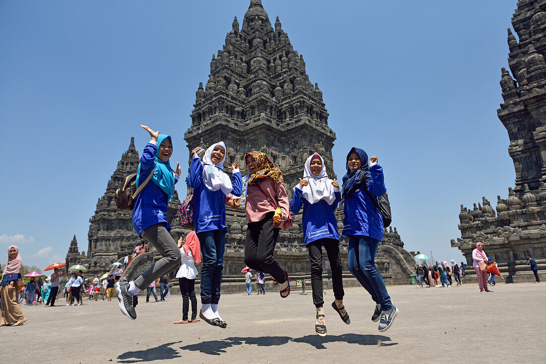 Schüler mit einem Lehrer mit farbigem Schal in der Mitte nehmen eine dynamische Pose während eines Schulausflugs zu den Prambanan-Tempelanlagen,UNESCO-Weltkulturerbe,Region Yogyakarta,Insel Java,Indonesien,Südostasien,Asien