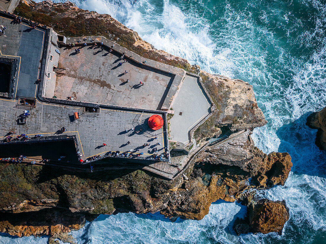 Drohnenansicht des Leuchtturms von Nazare von oben mit Wellen,die an die Felsen unter dem Turm schlagen,Nazare,Oeste,Estremadura,Portugal,Europa