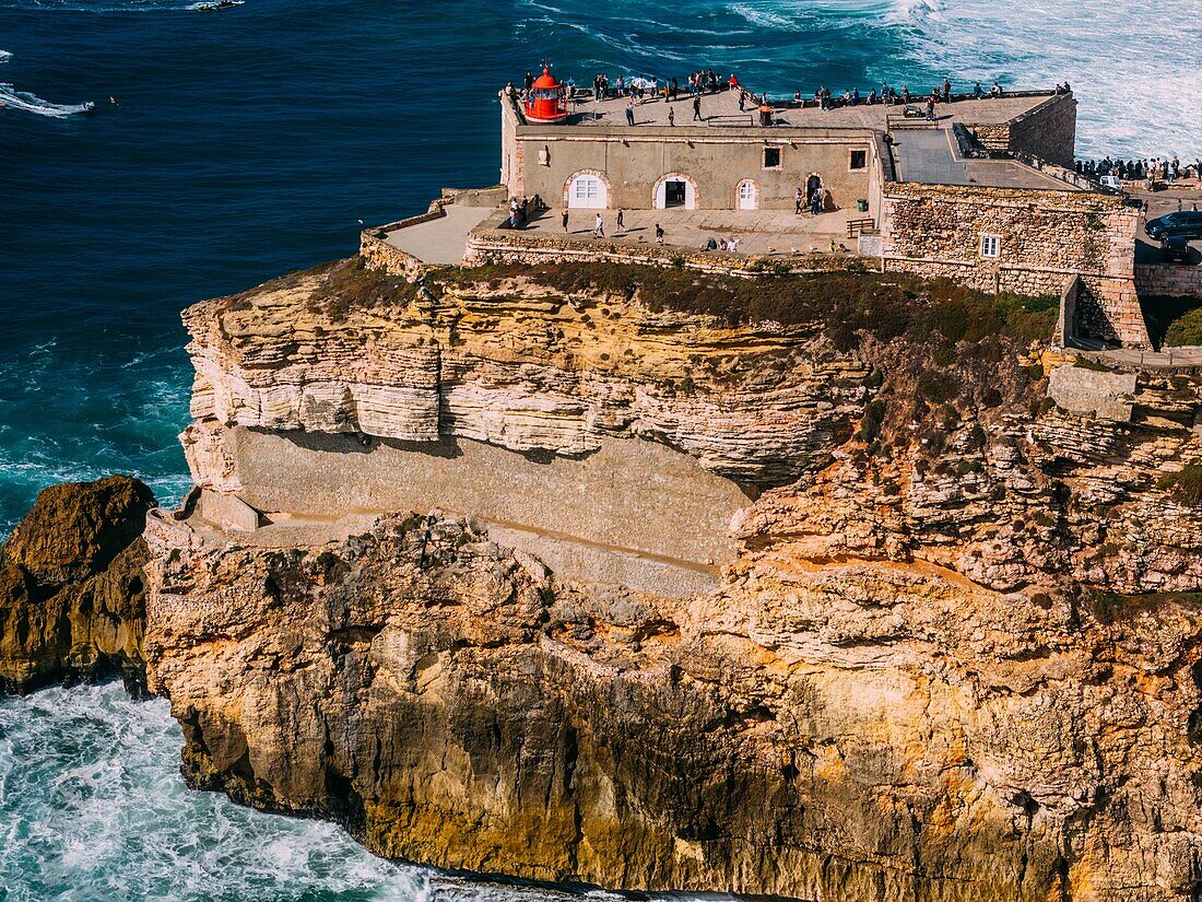 Luftaufnahme von Touristen am historischen Leuchtturm Sao Miguel Arcanjo mit Blick auf die atemberaubende Küste von Nazare mit riesigen Wellen,die spektakuläre Aussicht genießen,Nazare,Oeste,Estremadura,Portugal,Europa