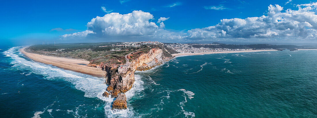 A breathtaking aerial drone panoramic view of Nazare's coastline with towering cliffs meeting the ocean, and waves crashing onto the sandy beach, Nazare, Oeste, Estremadura, Portugal, Europe