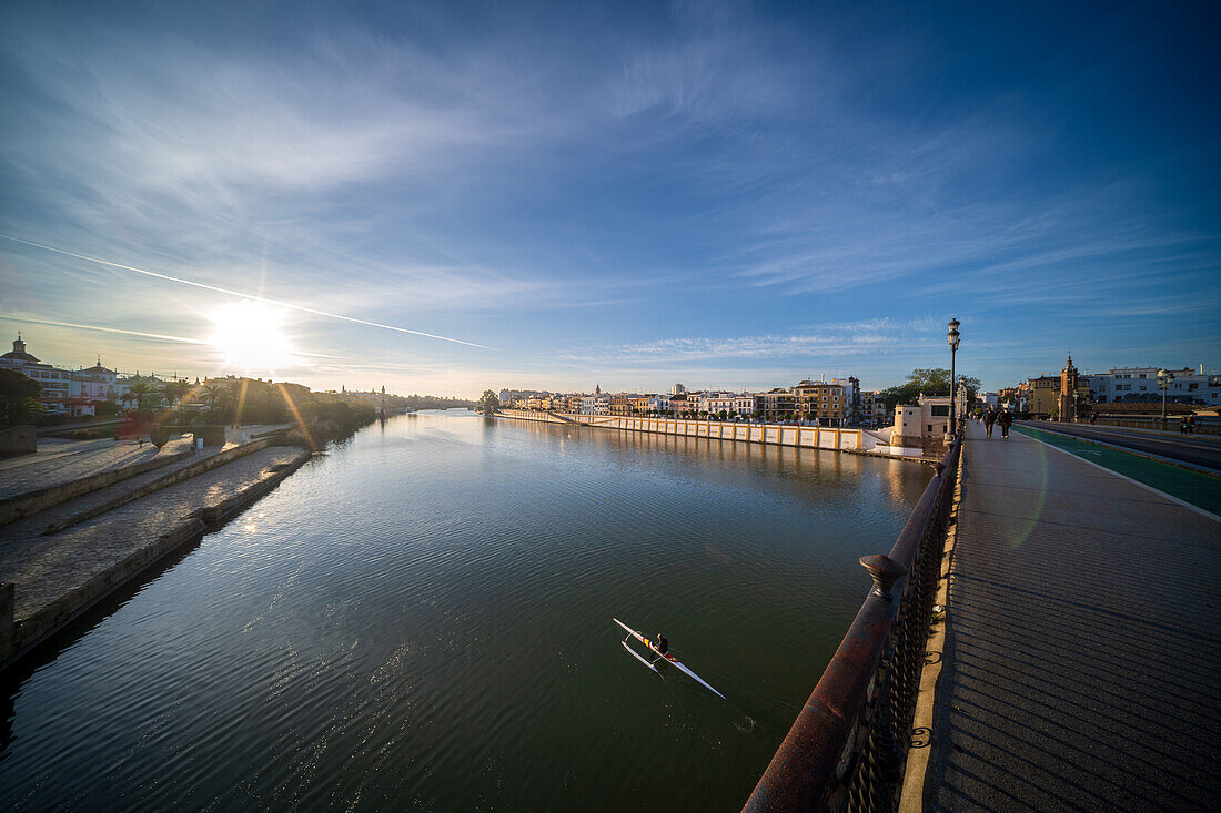 Capture of a serene sunrise over the Guadalquivir River, from the iconic Triana Bridge. The peaceful morning atmosphere reflects on the water alongside Betis Street.