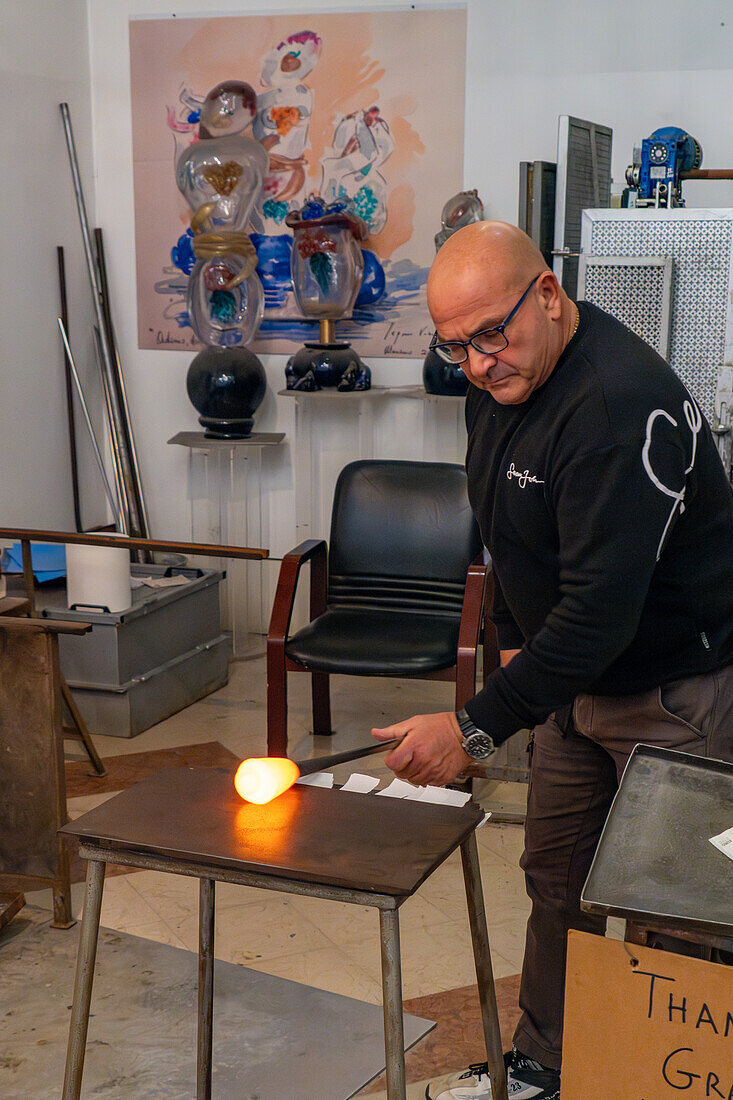 The glassblower rolls the molten gather on a marver in a glassblowing demonstration in Venice, Italy. Marvering creates a skin on the surface of the glass an begins to shape the gather.