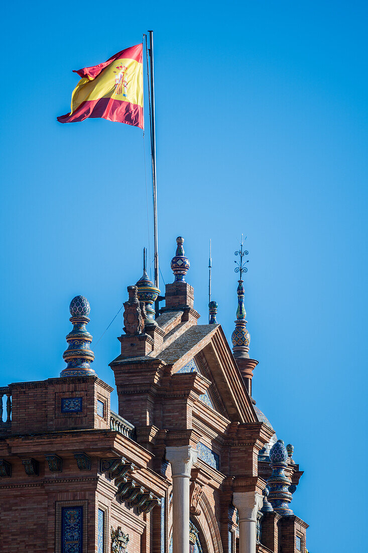 Close up of the intricate architectural details of Plaza de España in Seville, Spain, featuring traditional Spanish design elements and a vibrant flag against a clear blue sky.