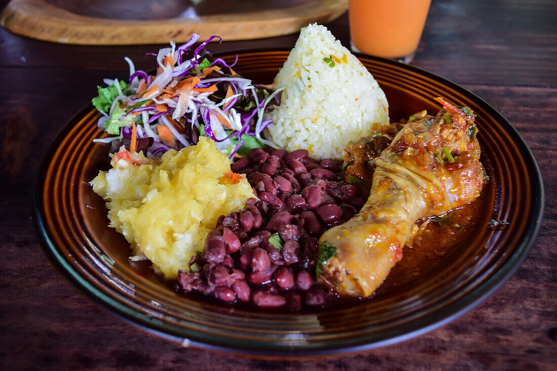 Casado dish with rice, chicken and peas, and fruit juice on table.