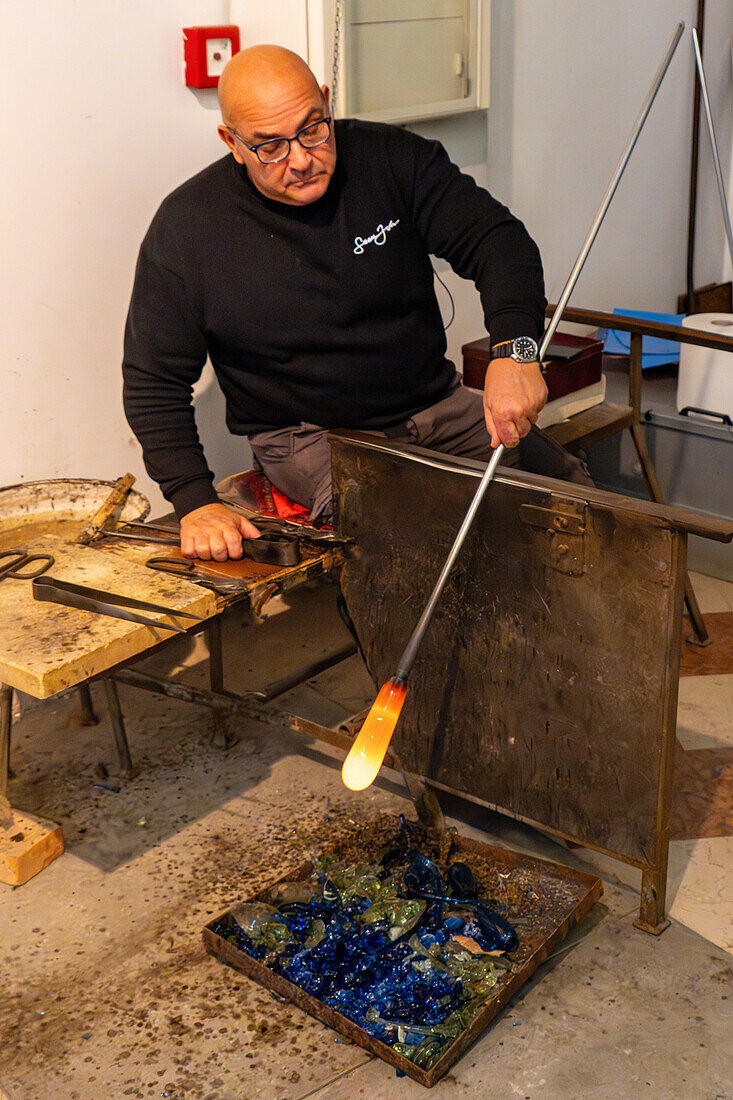 The glassblower rolls the gather and elongates it using gravity in a glassblowing demonstration in Venice, Italy.