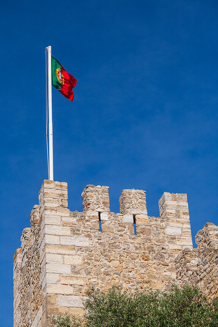 Majestic Saint George Castle showcases its battlements with the Portuguese flag soaring high against a vibrant blue sky.