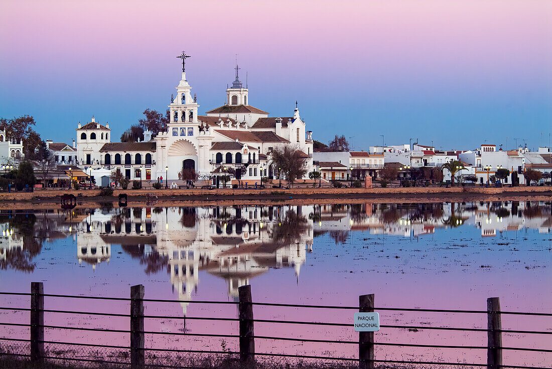 Scenic view of Ermita de la Virgen del Rocio reflecting in the serene marshland of Donana National Park, Spain during a colorful sunset.