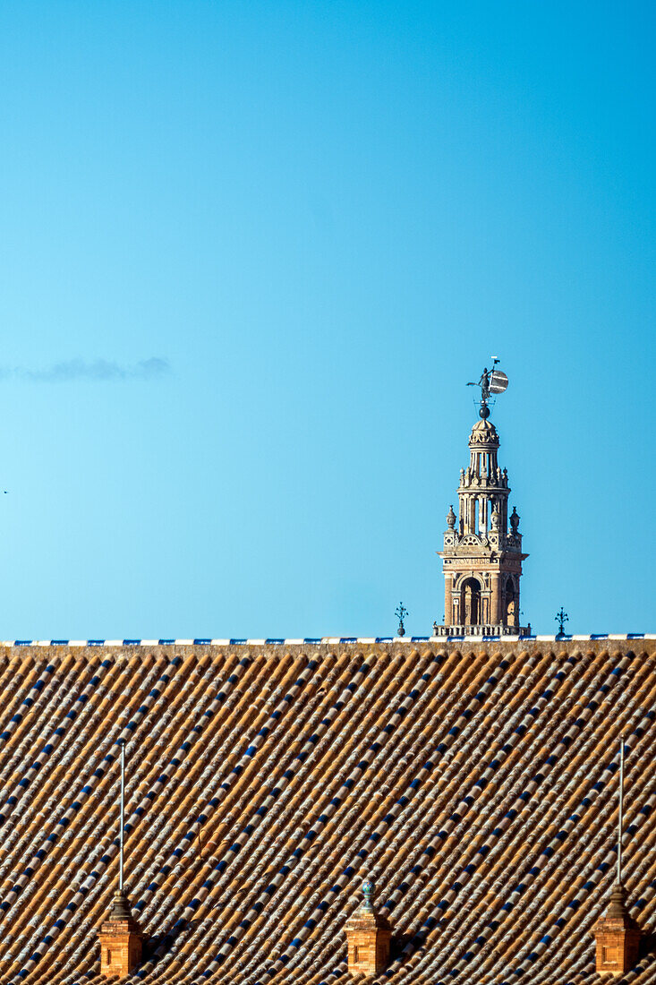 Ein klarer blauer Himmel über einem traditionellen Dach in Sevilla,Spanien,mit dem ikonischen Turm La Giralda im Hintergrund,der den historischen Charme der Stadt einfängt.