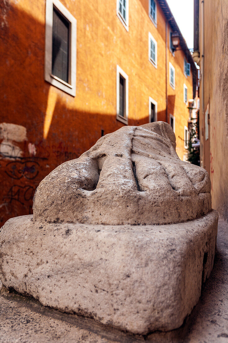 A massive foot of a historic Roman statue rests alongside a street in bustling Rome, showcasing ancient artistry and culture.